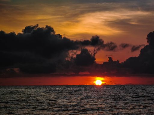 A breathtaking view of bright sun in dark cloudy sunset sky shining over the ocean