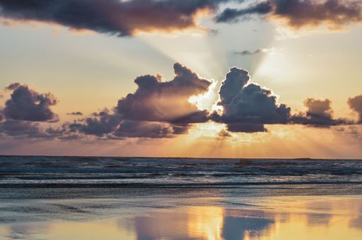 The bright sunlight in pink cloudy sunset sky shining over the sea seen from the shore