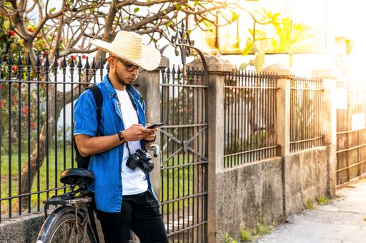 A male traveler wearing a hat, with photo camera checking his phone on the street