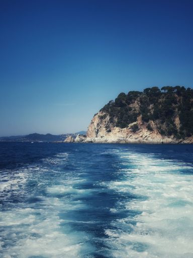 A vertical shot of boat trails on the water near the rocky Costa Brava in Spain