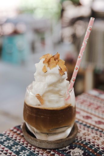 A vertical shot of an iced coffee with steam foam on top and a paper straw