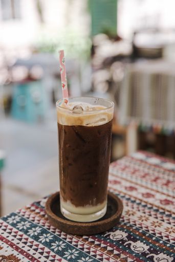 A vertical shot of an iced coffee with foam on top and a paper straw
