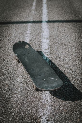 A vertical shot of an old black skateboard on the concrete ground