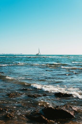 A vertical shot of a rocky seashore with mild waves and a boat on the background