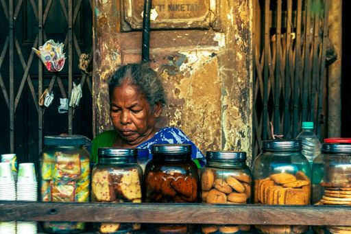 A portrait of an aged female tea seller sitting under an old building with variety of biscuits in front