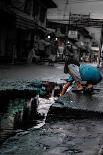 A vertical shot of a poor child playing with water from the rain in Angeles, Philippines