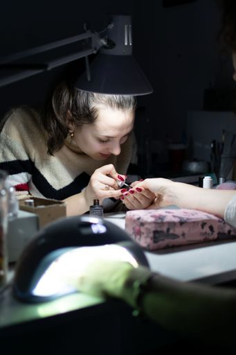 A Caucasian woman taking care of the nails of another person and applying gel nail polish