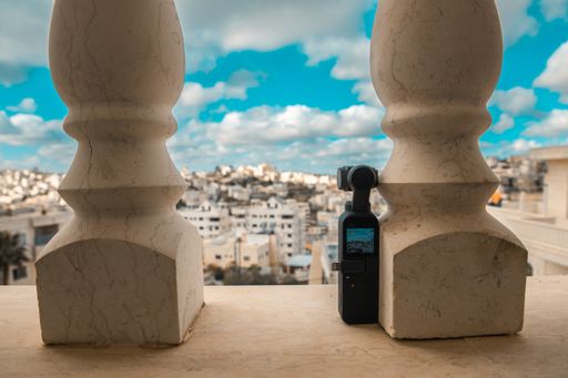 A closeup shot of a pocket camera  on a fence pointed at the cityscape