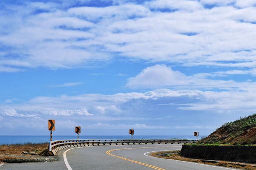 A beautiful view of a road by the sea under blue cloudy sky