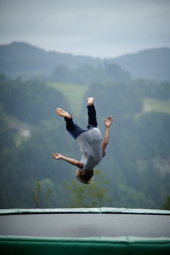 A vertical shot of a child jumping on a trampoline with mountains in the background