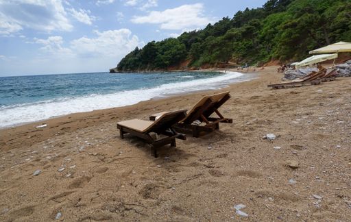 A sandy beach with two wooden chairs in front of the sea on a sunny day with a blue sky in the background, Budva, Montenegro