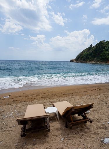 A vertical shot of two wooden chairs in front of the sea on a sunny day with a blue sky in the background, Budva, Montenegro