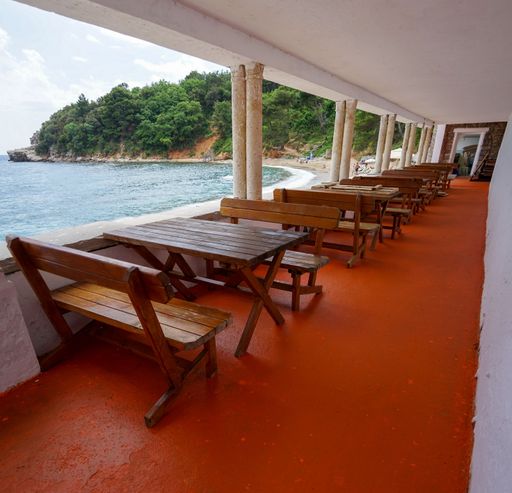 The inside of a beach cafe with wooden tables and chairs, with a blue cloudy sky in the background