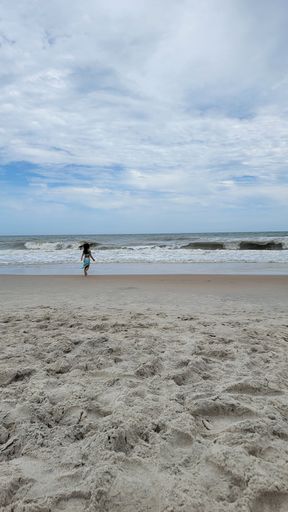 a vertical shot of a little girl on the beach