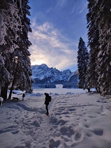 A vertical shot of a person walking on a snowy trail near the frozen Fusine Lake in Italy