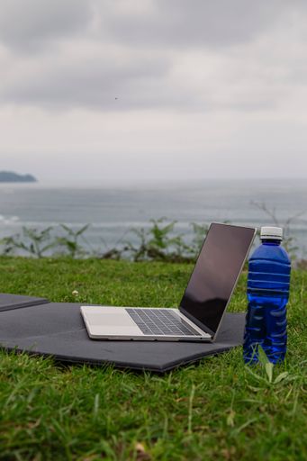 A laptop with a yoga mat, bottle of water outdoors. Online sports or yoga training concept.