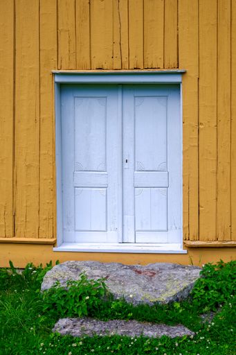A vertical shot of a wooden door in ochre yellow wall
