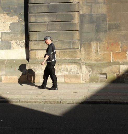 A male in a cap walking on a sidewalk in Glasgow on a sunny day