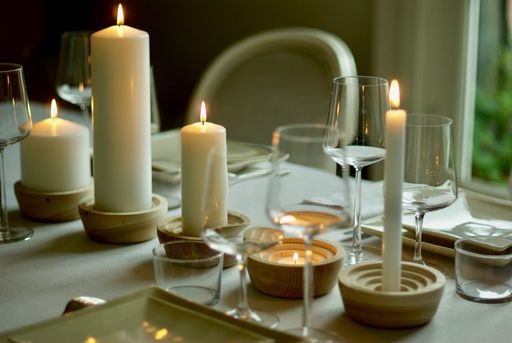 A closeup shot of a dinner table with white candles and wine glasses with a blurred background