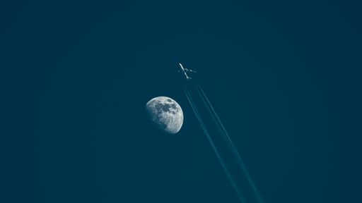 A low angle shot of an airplane flying through a dark blue sky with the huge moon beside it