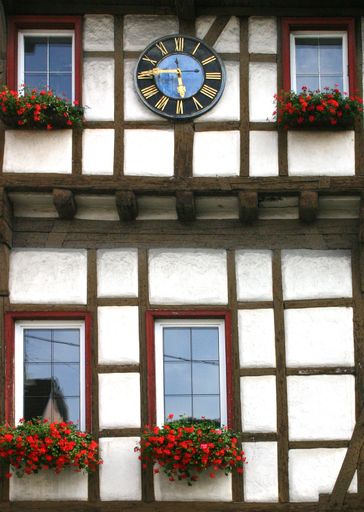 A vertical shot of a building with a vintage clock on top and red flowers on the window sills