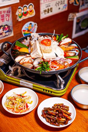 A vertical shot of bowl of gourmet ramen soup with vegetables on a mini stove near bowls of appetizers