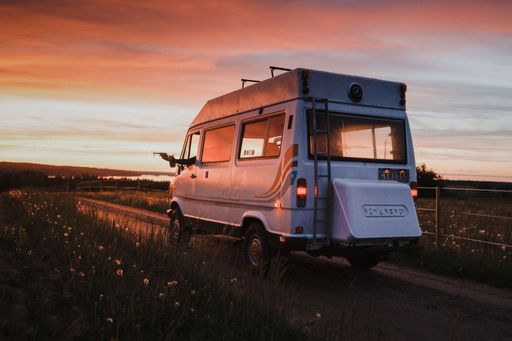 A eautiful scene of a van life car walkign on a road with lawns and flowers at sunset