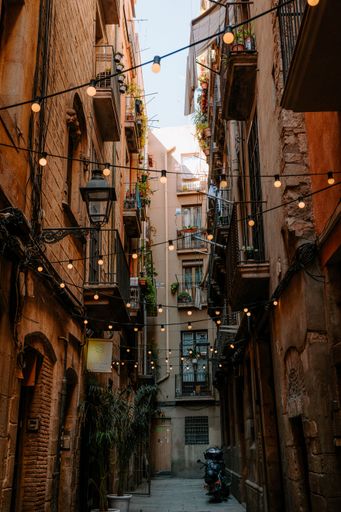 A vertical shot of a road between the buildings with bulbs hanging from the wire in Barcelona, Spain