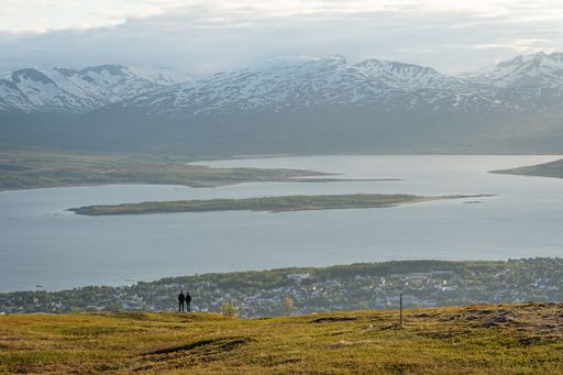 A scenic view of a couple on a green hill against a lake and a mountain range in Tromso, Norway