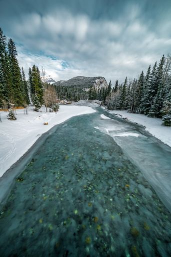 A vertical shot of a frozen turquoise river in an area covered with snow next to a forest