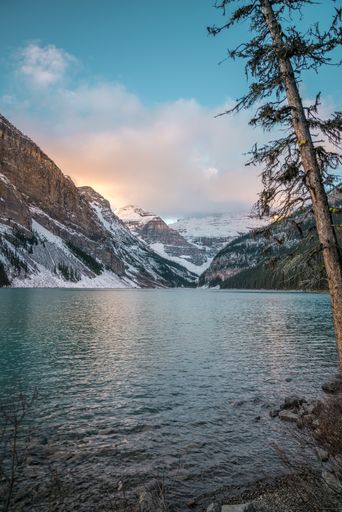 A vertical shot of a lake in the center of snowy mountains and the bright sky in the background