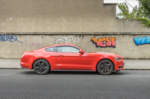 A red Ford Mustang parked in south Dublin, Ireland against a wall of graffiti