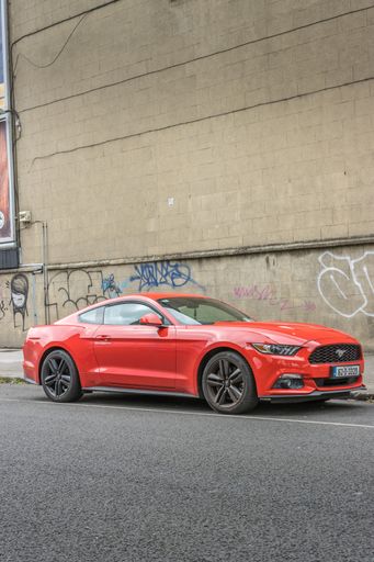 A vertical of a red Ford Mustang parked in south Dublin, Ireland against a wall of graffiti
