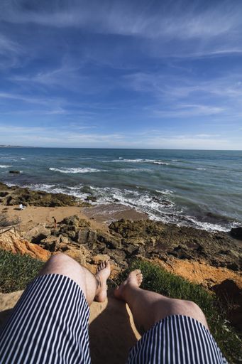 A vertical shot of the legs of a person sitting on rocks on the Chiclana beach, Cadiz, Spain