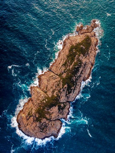 An aerial top view of a rocky Ng Fan Chau island washed by ocean waves