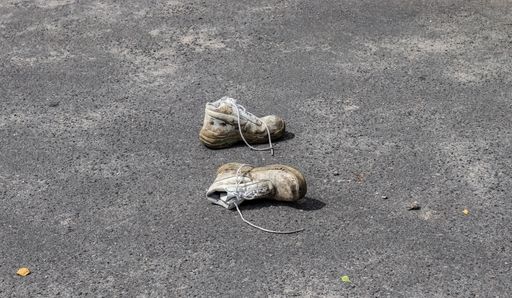 A high angle shot of a pair of old shoes abandoned on the asphalt