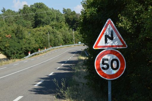A dangerous turn warning sign with 50 Kilometers speed sign against trees and sky