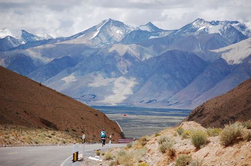 A landscape view with two cyclists riding to snowy mountain range background