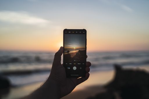 A person taking a picture of the sea during the sunset with a phone in Cala de Roche, Spain