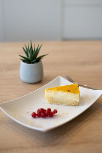 A vertical closeup shot of a slice of mango cake with berries on the white minimalistic plate
