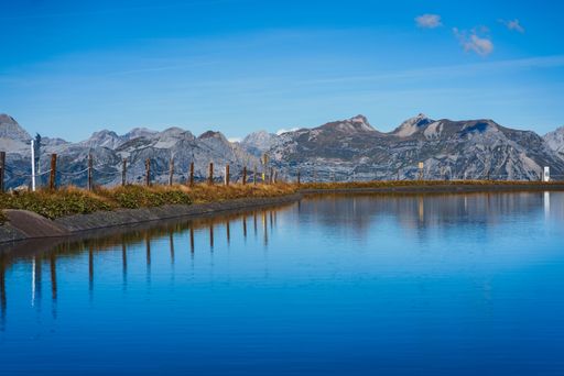 A scenic shot of mountains and vegetation reflecting on the Speicherteich Kapell in Austria