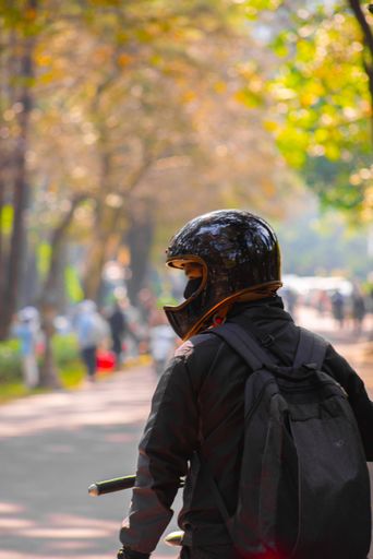 A vertical shot of a young motorcyclist in a park wearing a helmet