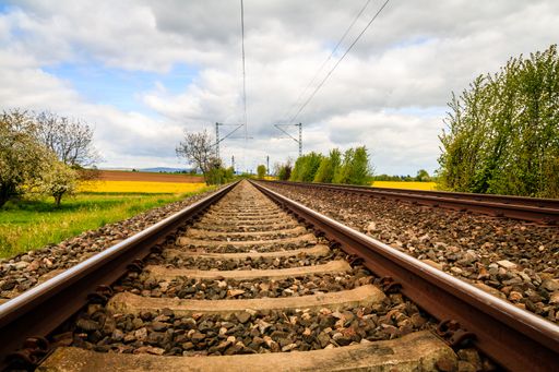A low-angle shot of a railway in the middle of farm fields under a cloudy blue sky