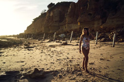 A beautiful shot of a female in swimsuit walking on a shore during sunset