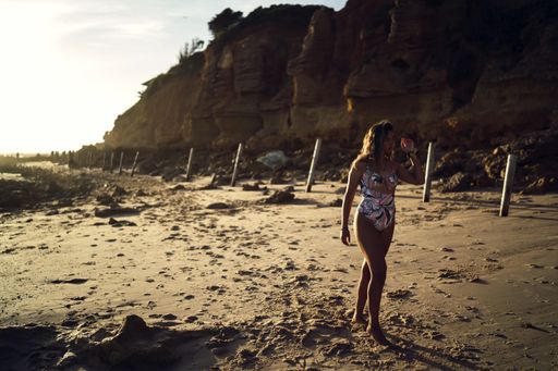 A beautiful shot of a female in swimsuit walking on a shore during sunset