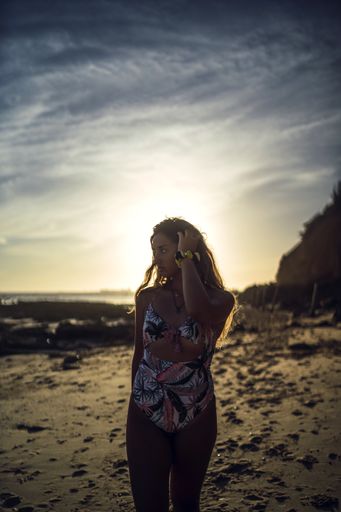A vertical shot of a female in swimsuit walking on a shore during sunset