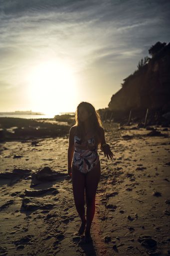 A vertical shot of a female in swimsuit walking on a shore during sunset