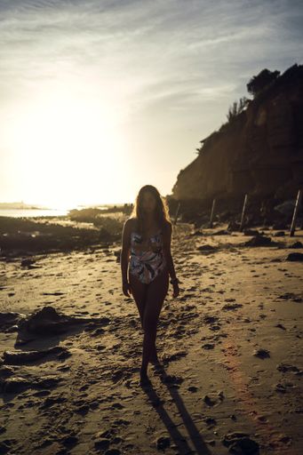 A vertical shot of a female in swimsuit walking on a shore during sunset