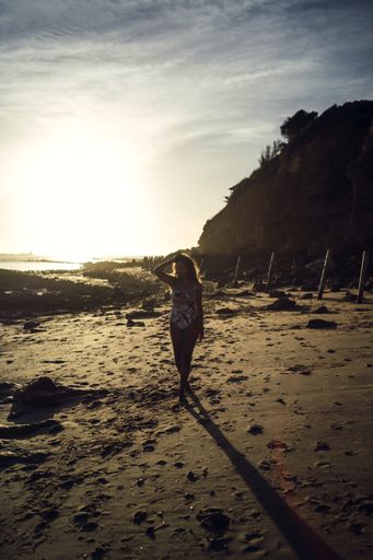 A vertical shot of a female in swimsuit walking on a shore during sunset