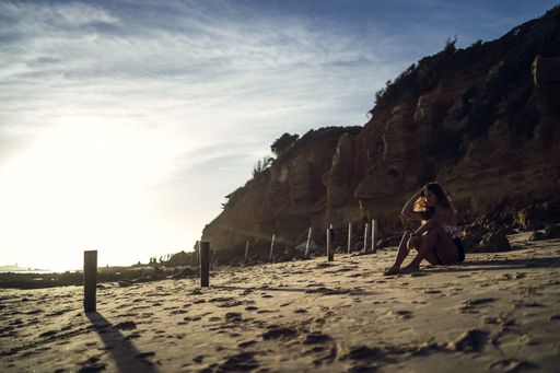 A young female in swimsuit sitting on sands on background of a cliff